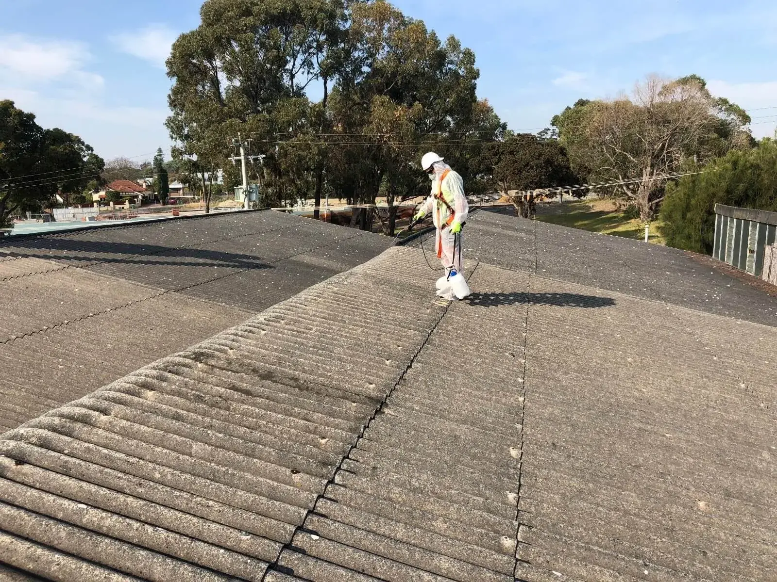 Worker in protective suit inspecting an asbestos cement roof