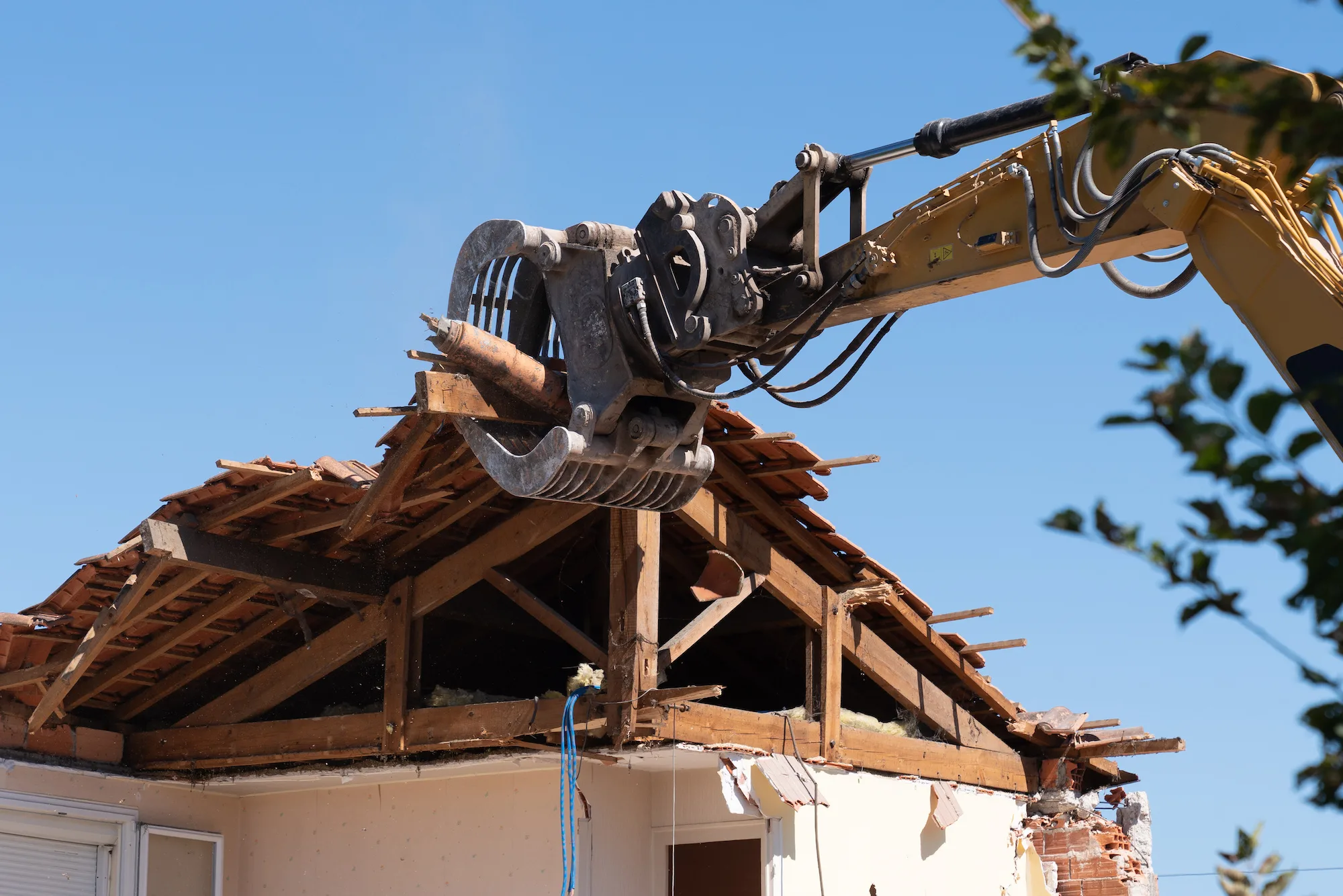 Excavator grab removing the timber roof frame of a house