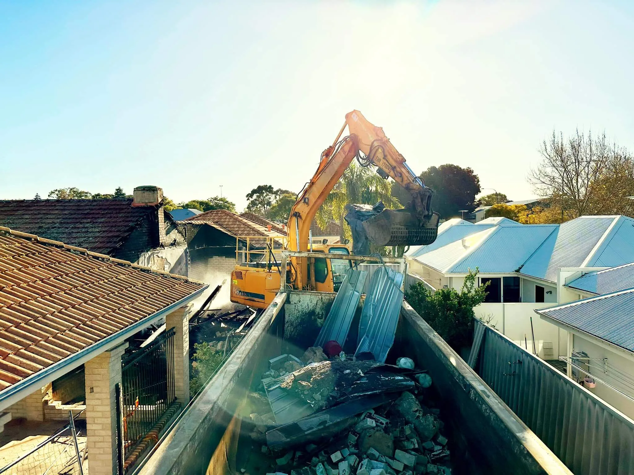 Excavator demolishing a house between neighbouring homes